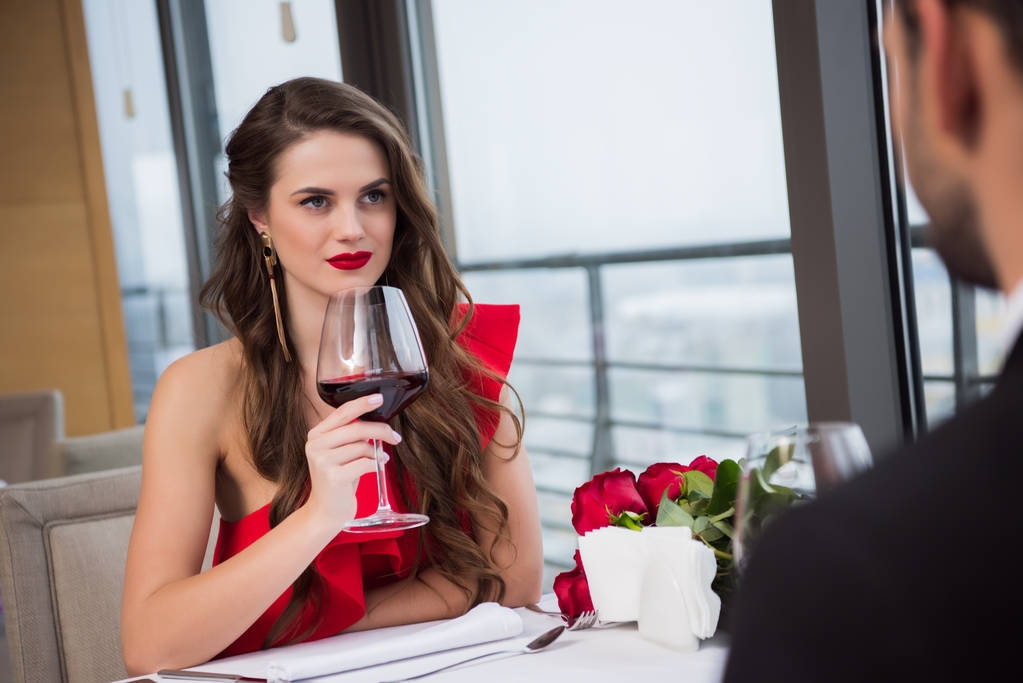 Frau mit Glas Rotwein schaut Freund beim Valentinstag-Date im Restaurant an - Foto, Bild