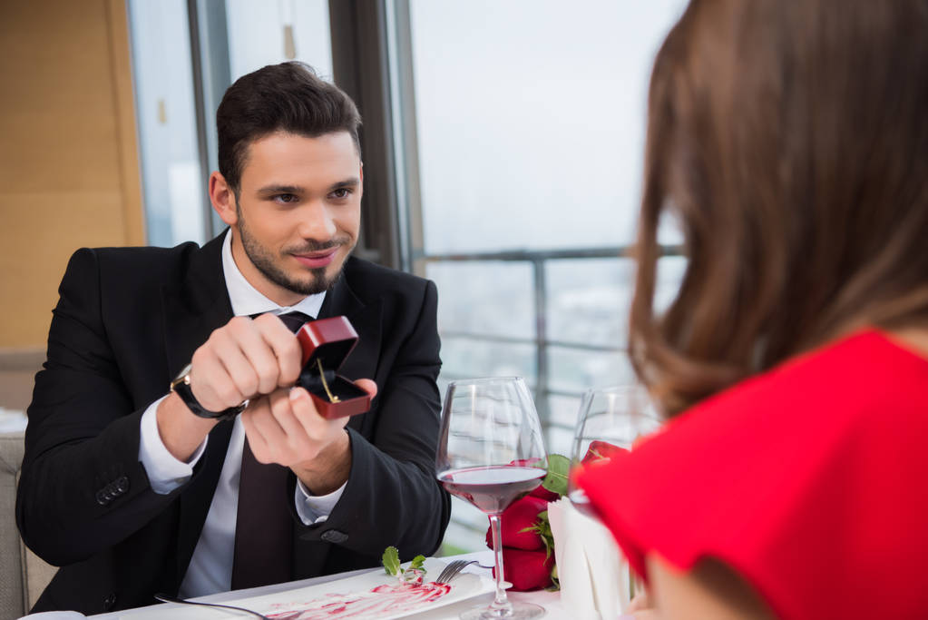 visão parcial do jovem que apresenta o presente à amiga na data romântica no restaurante
 - Foto, Imagem