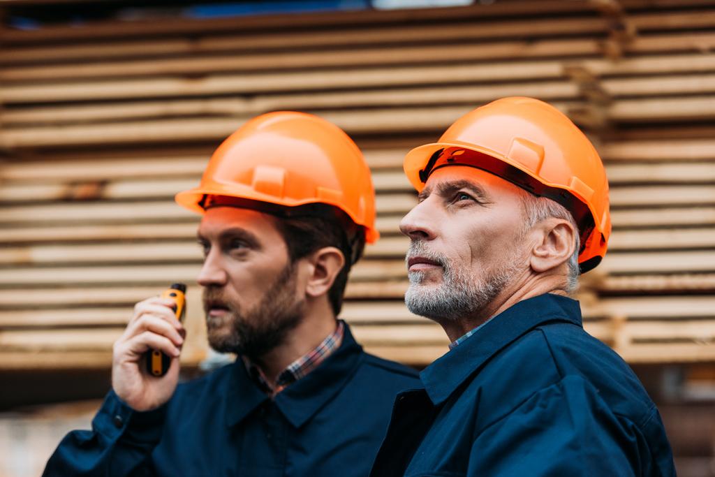 two builders in helmets working with walkie talkie outside on construction - Photo, Image