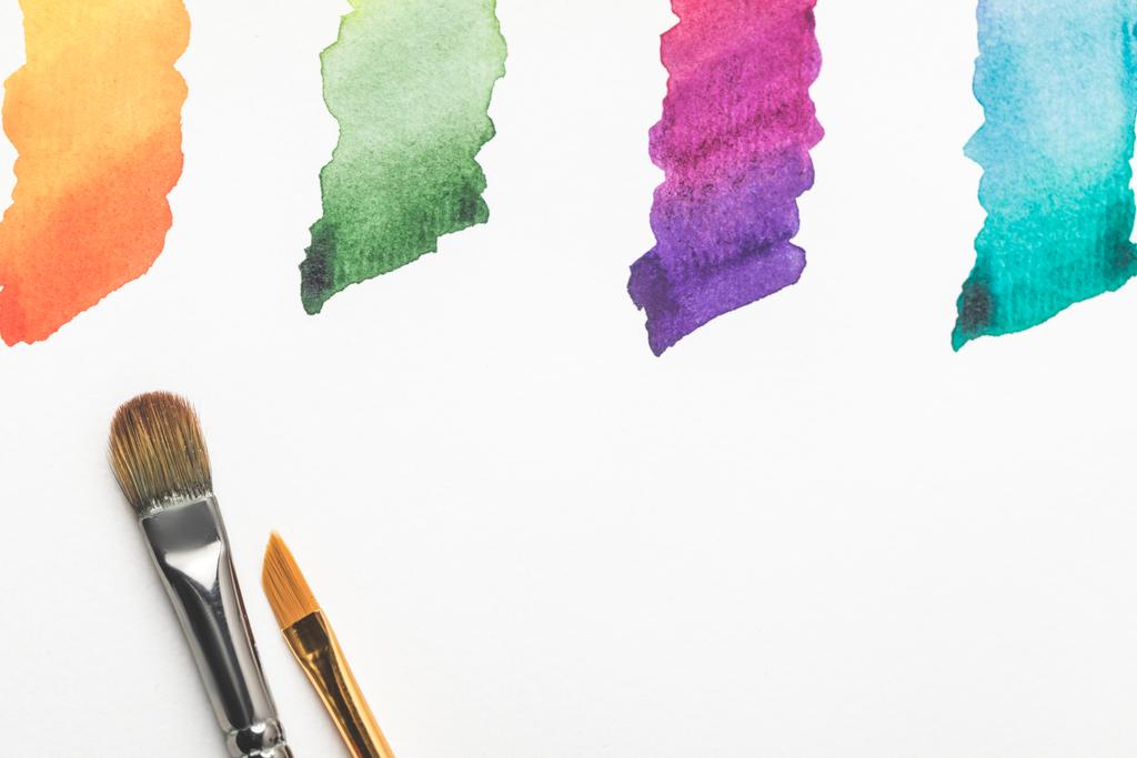 Крупный план кистей и красочных ярких мазков краски, выделенных на белом
 - Фото, изображение