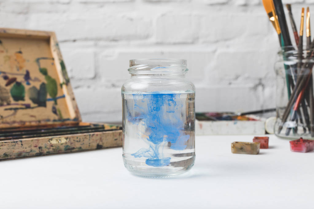 close-up view of glass jar with water and blue paint at designer workplace - Photo, Image