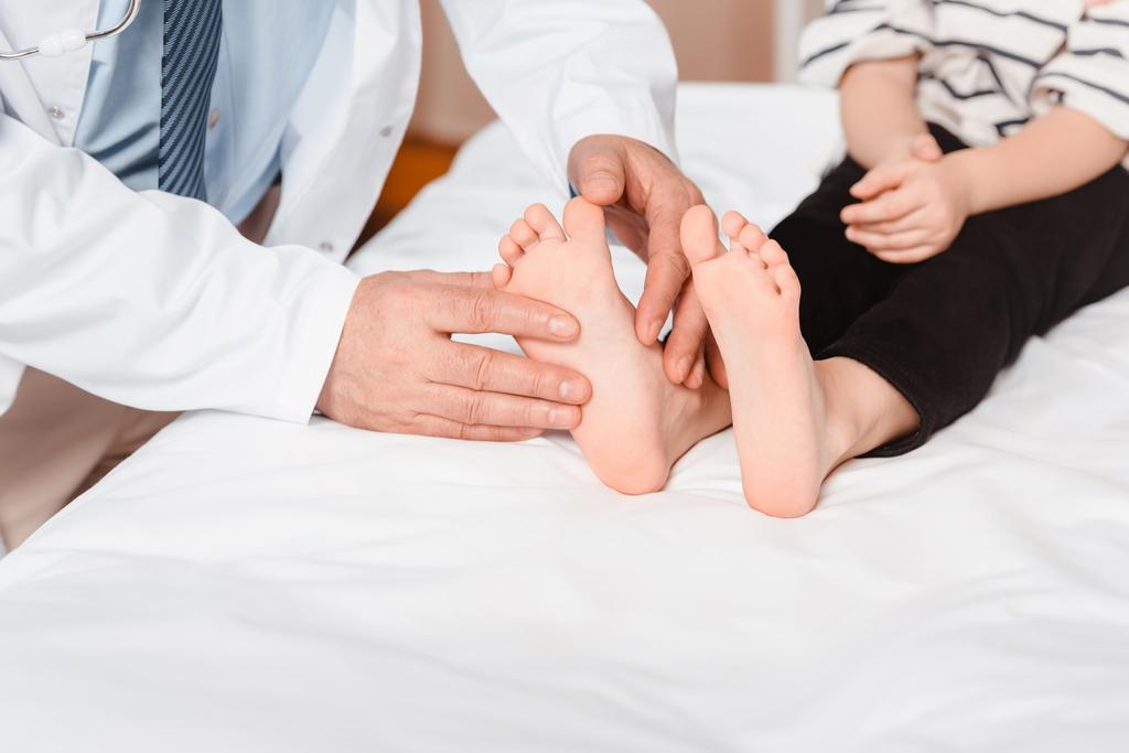 病院で子供の足を調べる医師のショットをトリミング - 写真・画像