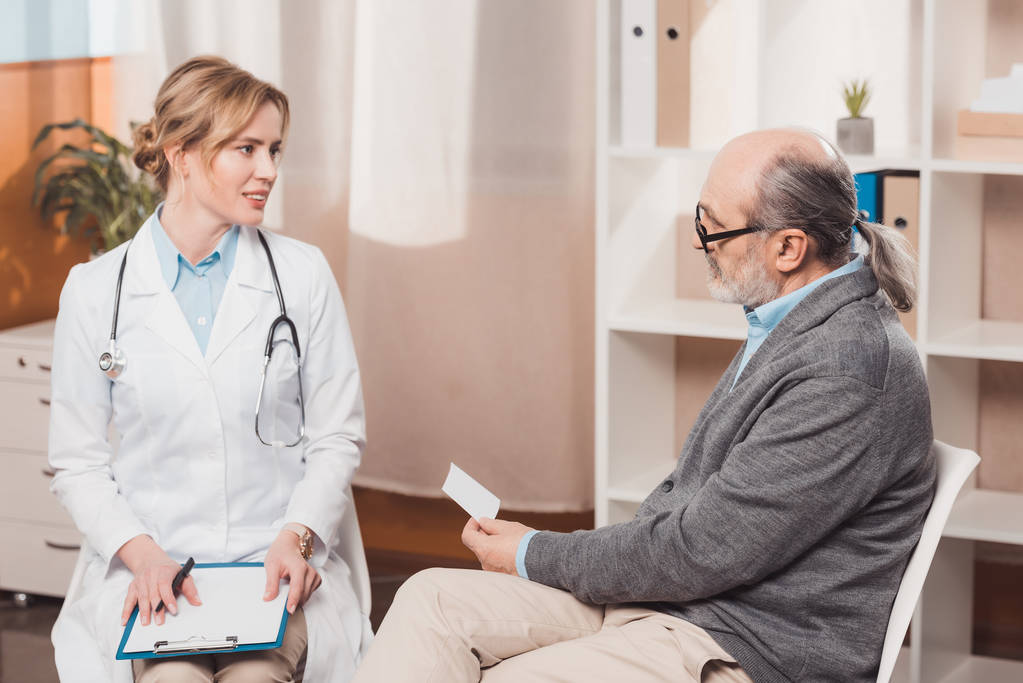 γιατρός σε λευκό παλτό με το notepad, ακούγοντας την καταγγελία ασθενών στην κλινική - Φωτογραφία, εικόνα