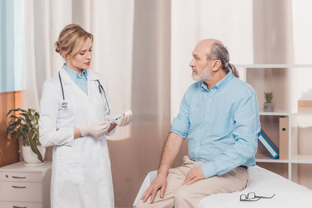 Portret van doctor in de witte vacht gaan injectie aanbrengen senior patiënt in kliniek - Foto, afbeelding