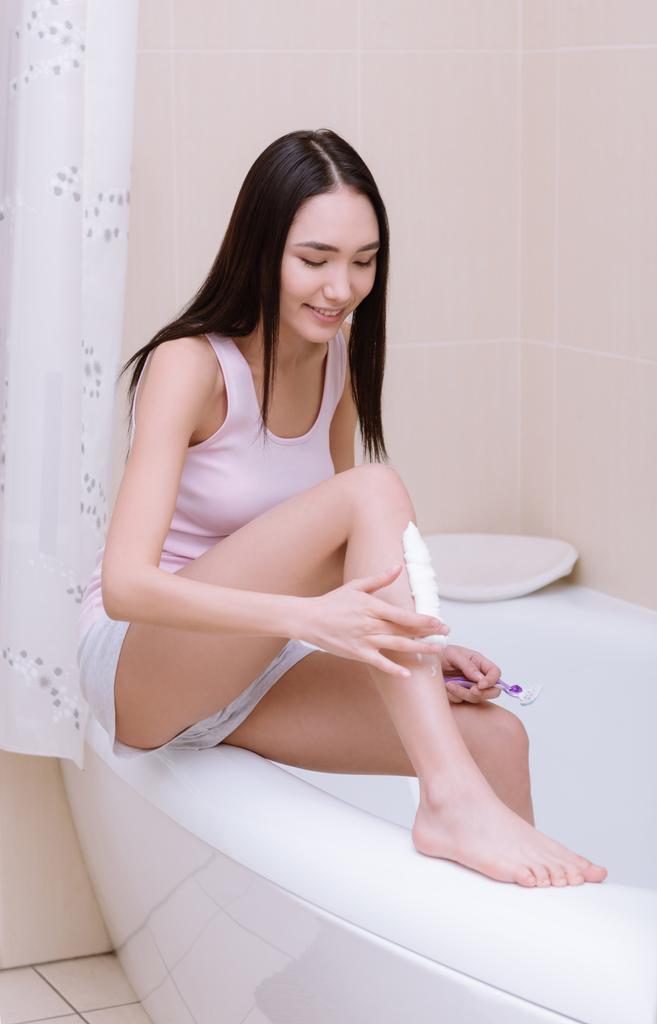 Uśmiechnięta dziewczyna azjatyckich golenie nóg w łazience  - Zdjęcie, obraz