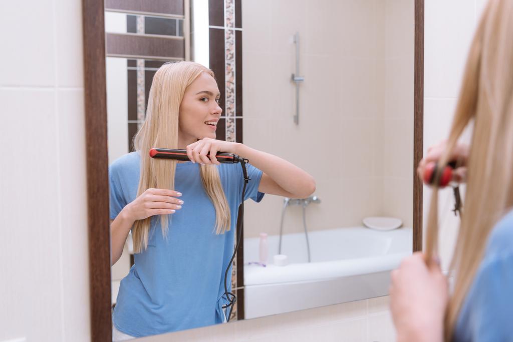 усміхнена дівчина випрямляє волосся у ванній з праскою для волосся
 - Фото, зображення