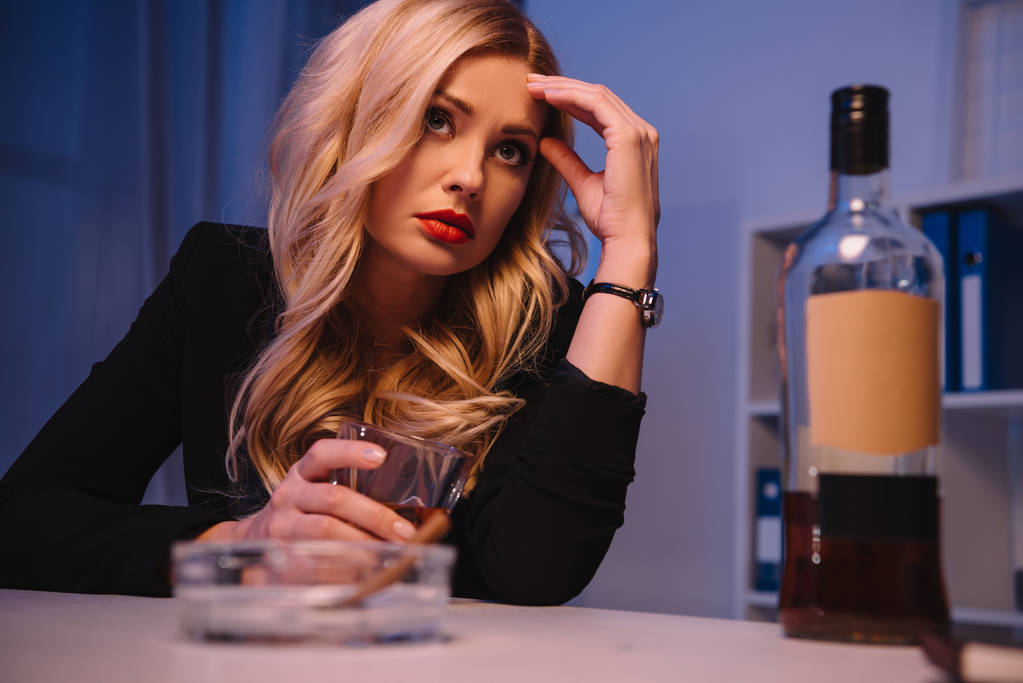 уставшая блондинка-бизнесвумен сидит за столом со стаканом виски
 - Фото, изображение