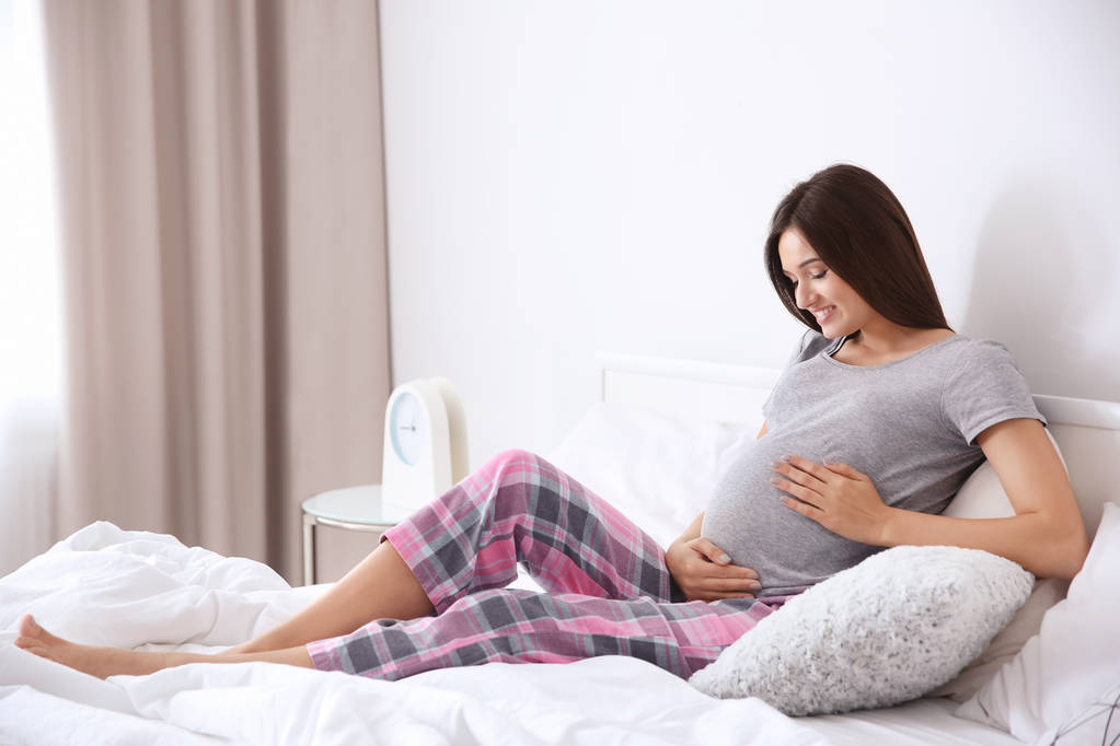 Jonge zwangere vrouw die thuis op bed zit - Foto, afbeelding