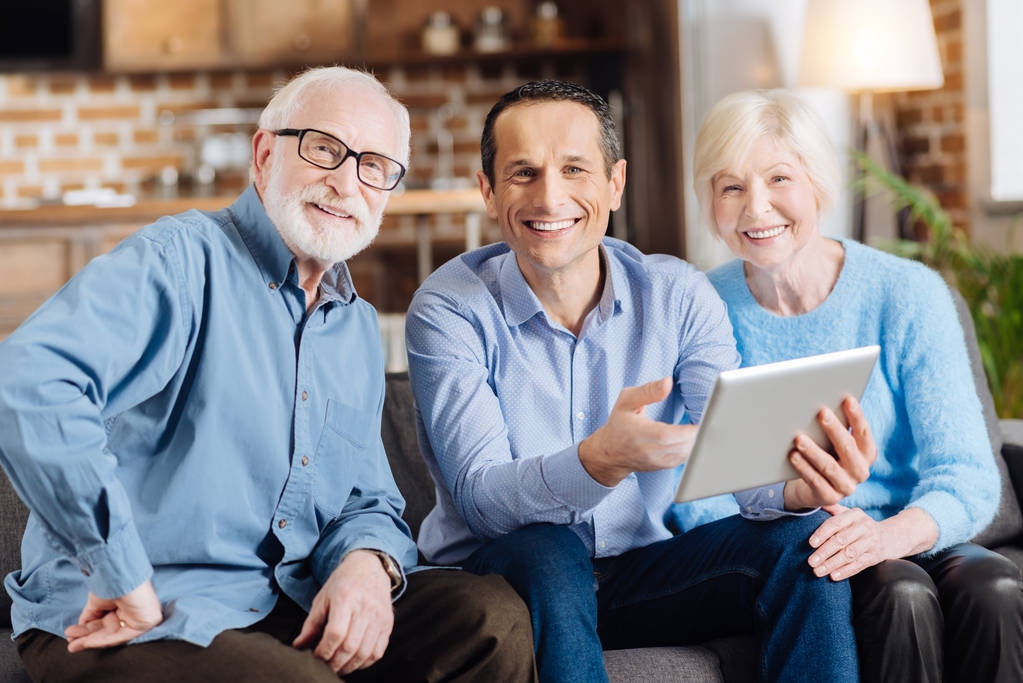 Молодой человек и его пожилые родители позируют во время использования планшета
 - Фото, изображение