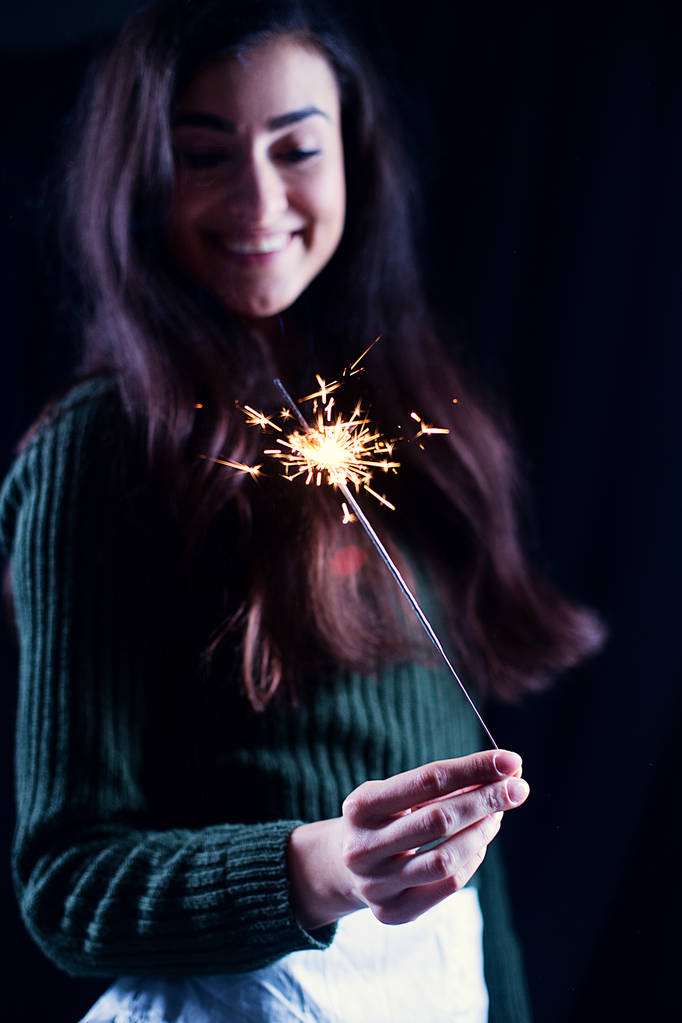Ragazza felice sorridente e tenendo in mano un fuoco d'artificio scintillante. Ragazza sullo sfondo intenzionalmente blured. Il concetto di celebrare il nuovo anno e il Natale
. - Foto, immagini