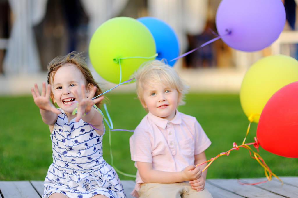 Маленький хлопчик і дівчинка розважаються і святкують день народження з барвистими повітряними кулями
 - Фото, зображення