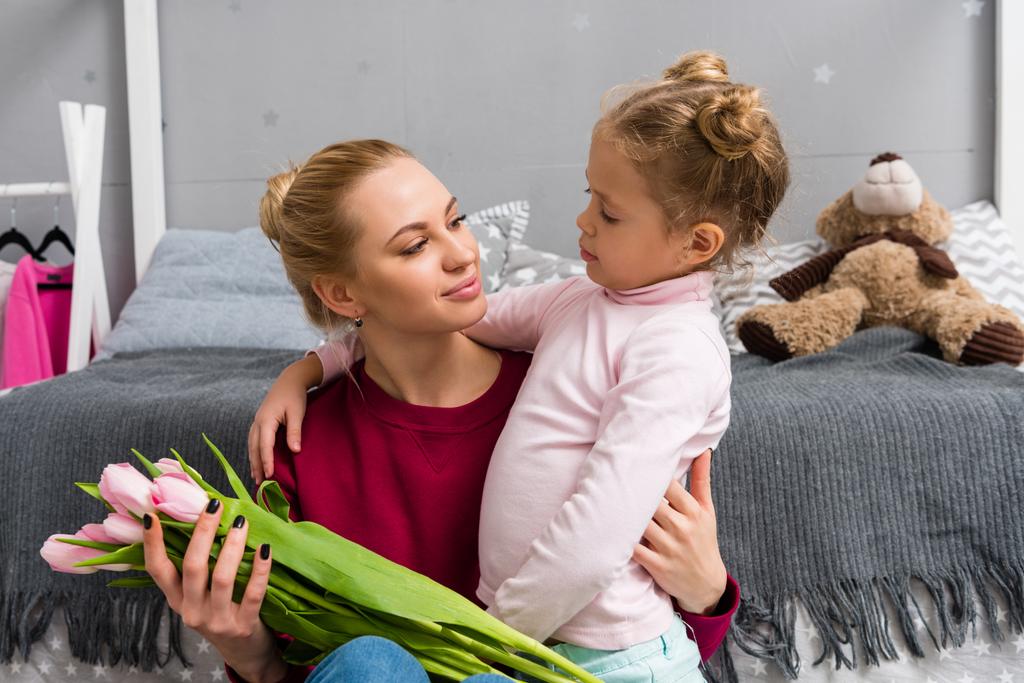 adorable little daughter presenting tulips bouquet for mother on mothers day - Photo, Image