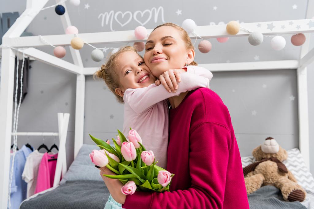 Tochter überreicht Tulpenstrauß für Mutter am Muttertag und umarmt sie - Foto, Bild