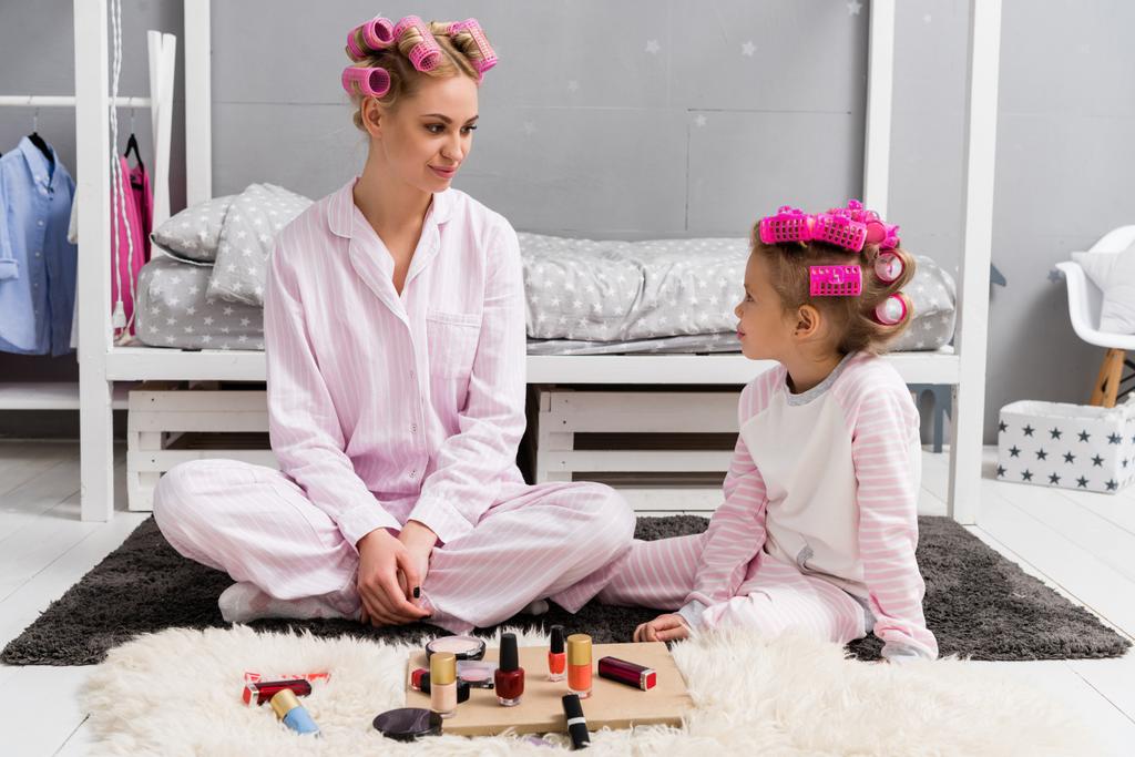 mother and daughter in pajamas with hair rollers on head sitting on floor - Photo, Image