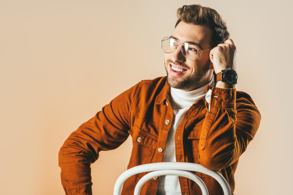 портрет счастливого человека в модной одежде и очках, смотрящего вдаль на бежевый
 - Фото, изображение