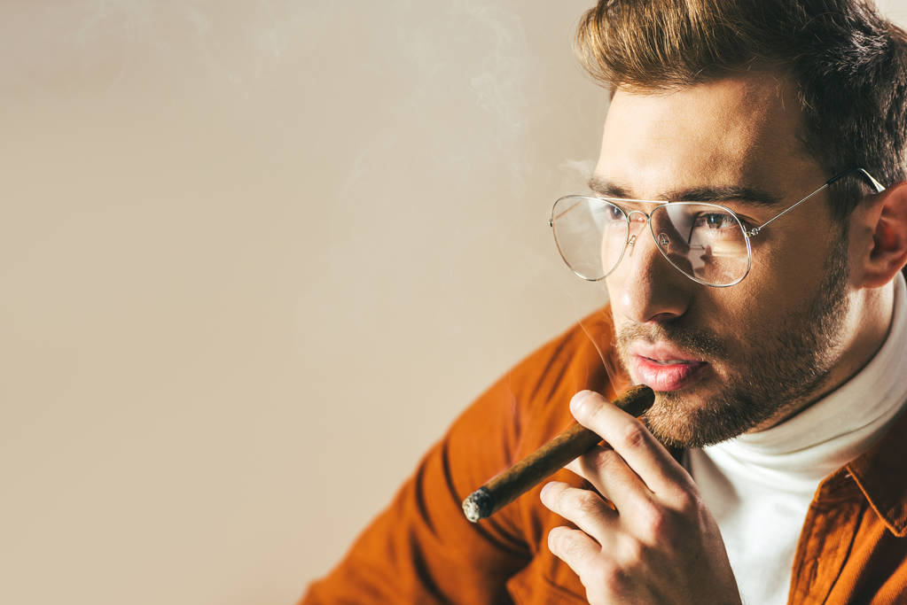 ritratto di uomo alla moda pensoso fumare sigaro e distogliere lo sguardo isolato sul beige
 - Foto, immagini
