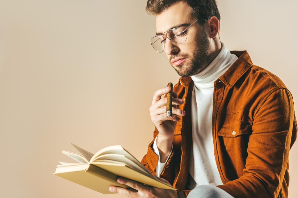 Πορτραίτο νεαρού άνδρα με πούρο ανάγνωση βιβλίων που απομονώνονται σε μπεζ - Φωτογραφία, εικόνα