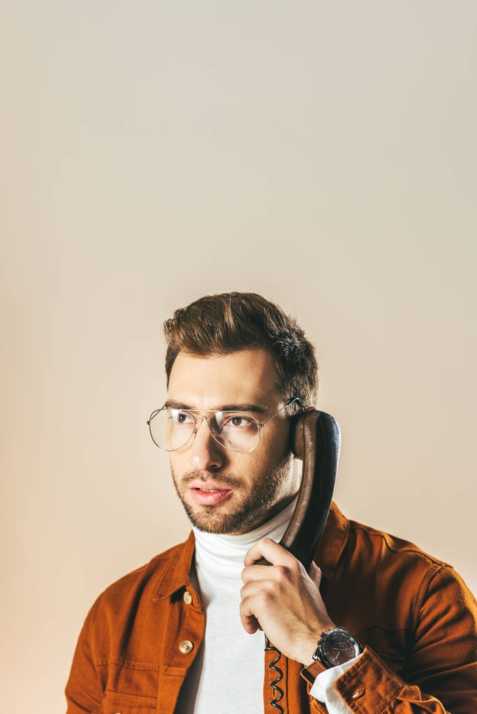 Telefonla konuşurken uzak bakan dalgın şık adam portresi üzerinde bej izole - Fotoğraf, Görsel