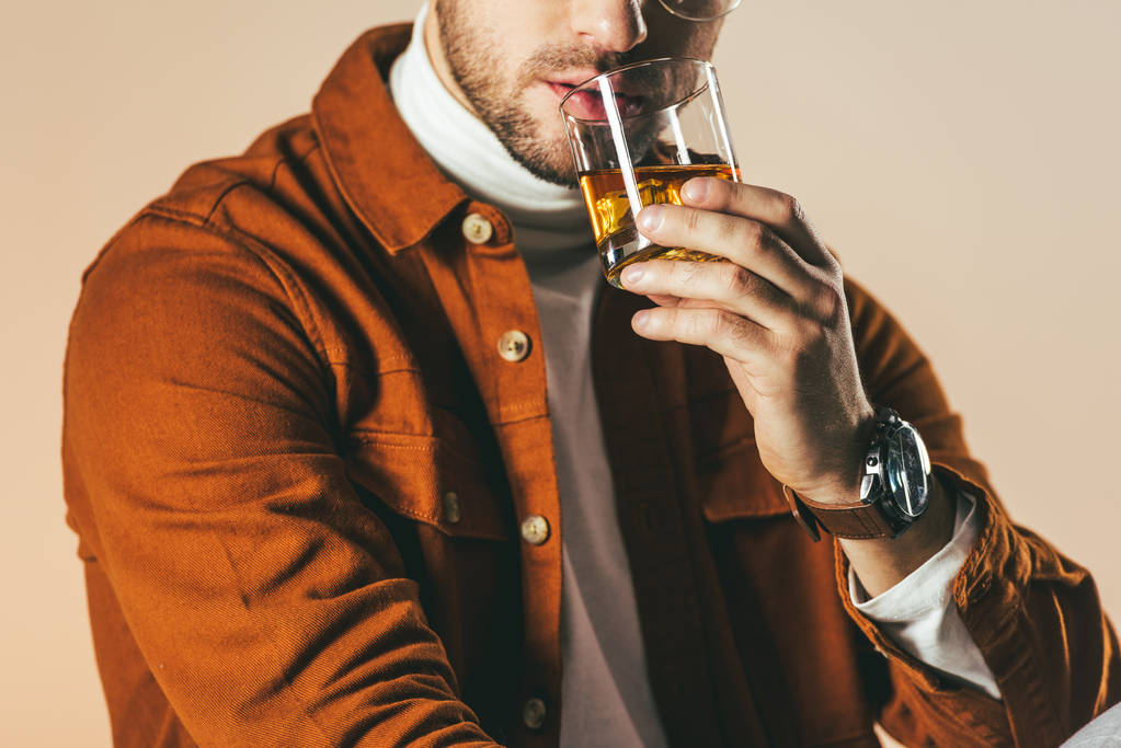 частичный вид человека в стильной одежде со стаканом виски в руке, изолированным на бежевом
 - Фото, изображение