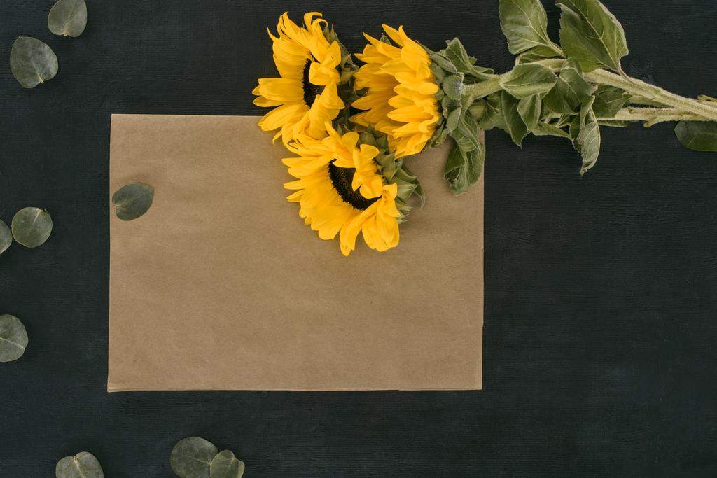 top view of blank paper envelope with sunflowers over black background - Photo, Image