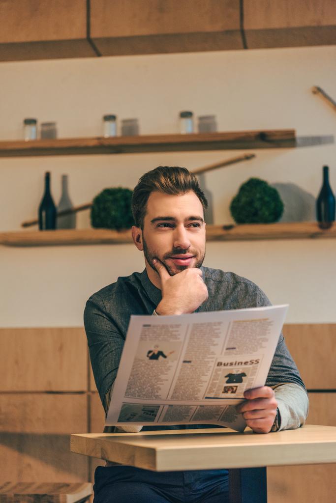 Portret van peinzende zakenman op zoek weg tijdens het lezen van de krant aan tafel in café - Foto, afbeelding