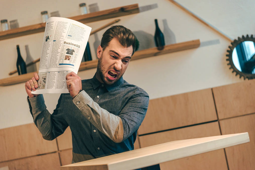 портрет разгневанного бизнесмена, бросающего газету за столик в кафе
 - Фото, изображение