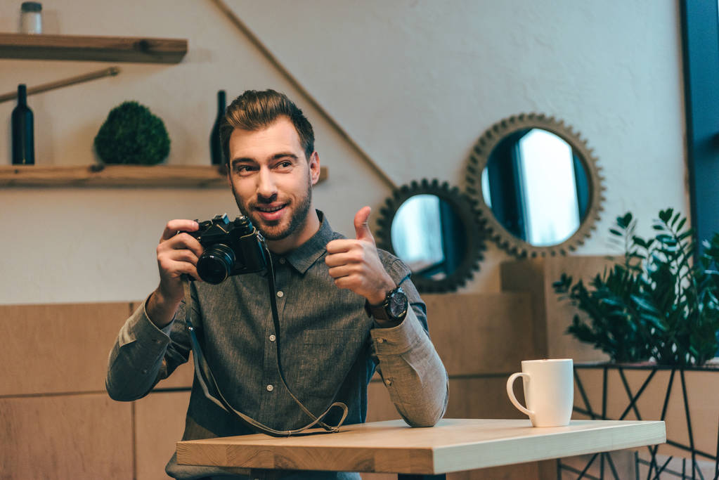 muotokuva nuori mies valokuva kamera osoittaa peukalo ylös kahvilassa
 - Valokuva, kuva