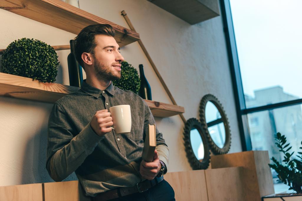 retrato del hombre sonriente con taza de café y libro en las manos en la cafetería
 - Foto, Imagen