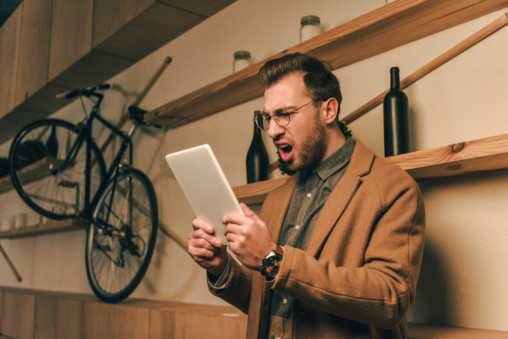 Zijaanzicht van boos stijlvolle man kijken naar tablet in handen in café - Foto, afbeelding
