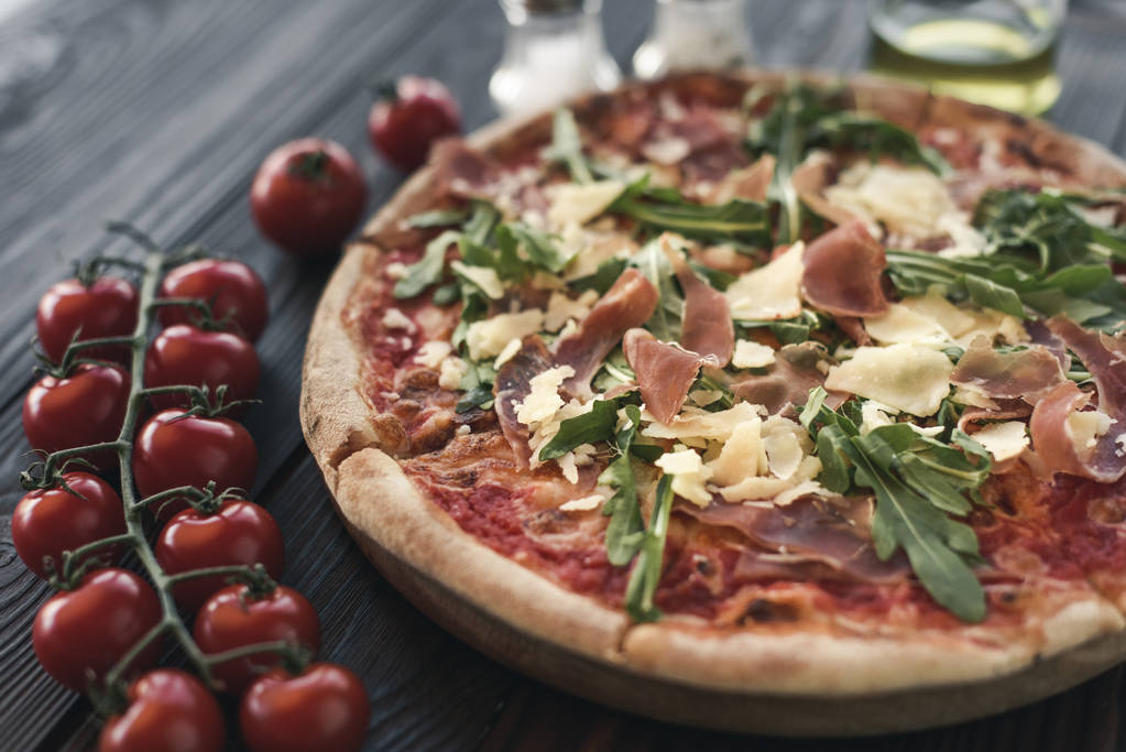 foco seletivo de pizza italiana, tomate cereja, especiarias e azeite em mesa de madeira
 - Foto, Imagem