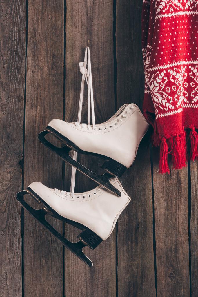 par de patines blancos y bufanda roja colgando en la pared de madera
 - Foto, imagen