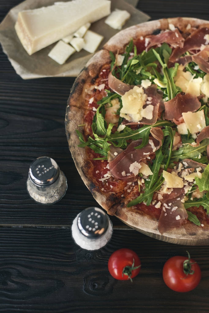 Close-up van pizza, specerijen en bestek op donkere houten oppervlak - Foto, afbeelding