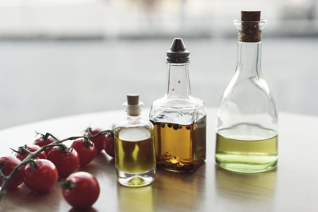 Nahaufnahme verschiedener Ölsorten in Flaschen und frischen Kirschtomaten - Foto, Bild