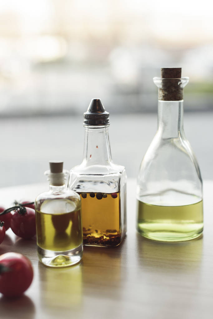 vista de perto de vários tipos de óleo em garrafas e tomates cereja frescos
 - Foto, Imagem