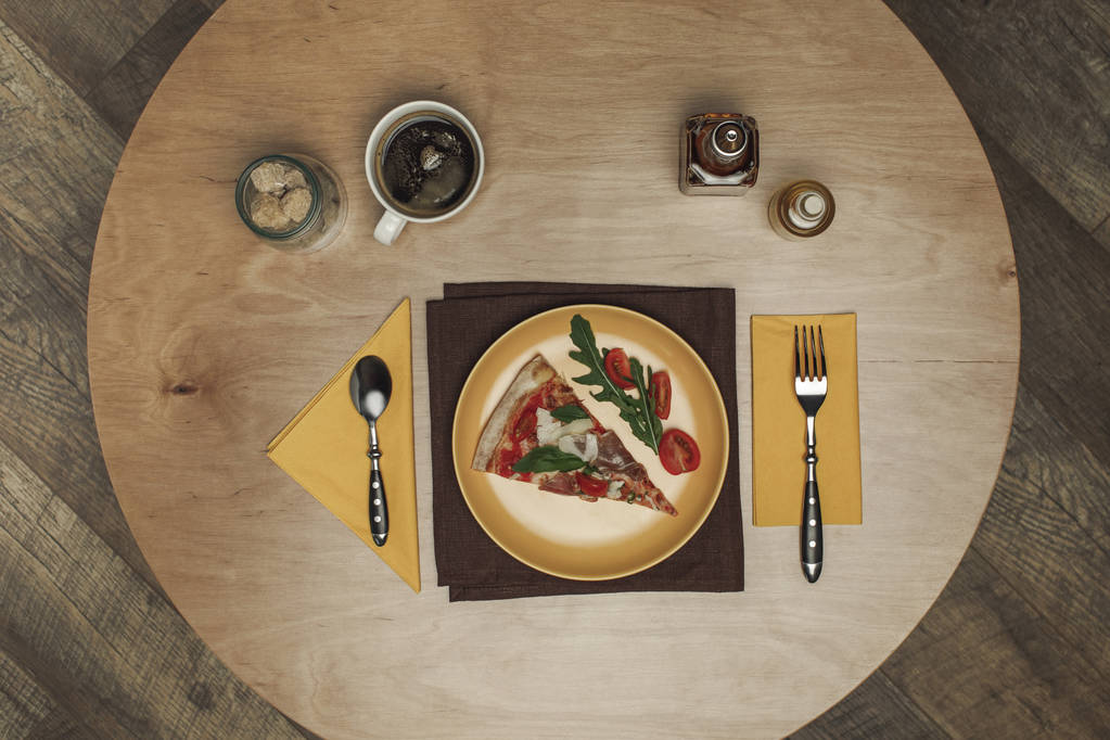 tendido plano con pedazo arreglado de pizza en el plato, taza de té y cubiertos en la mesa de madera
 - Foto, imagen
