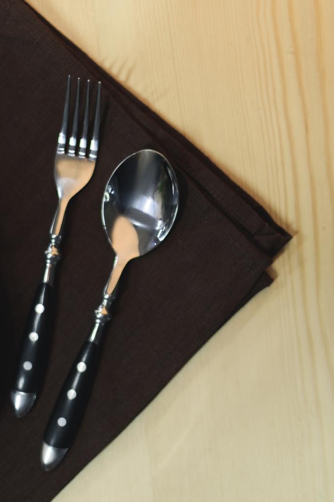 close up view of steel fork and spoon on napkin on wooden tabletop - Photo, Image