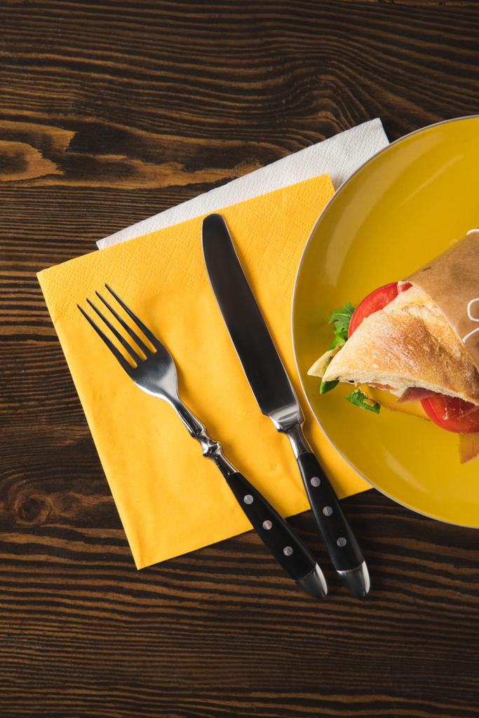 bovenaanzicht van sandwich op gele plaat met mes en vork - Foto, afbeelding
