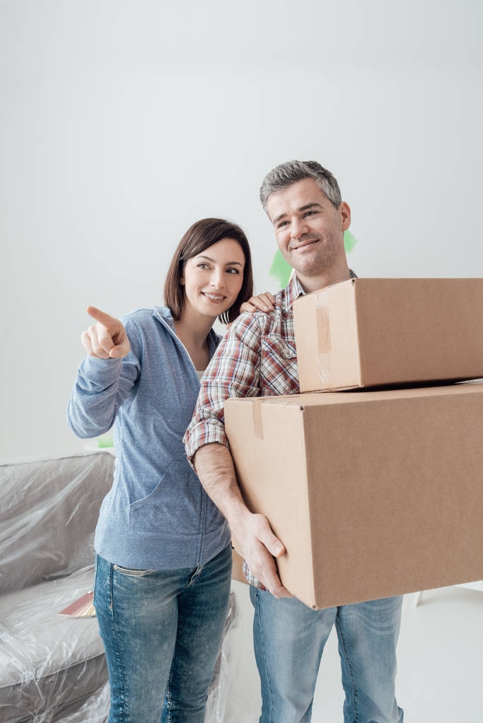 Pár stěhování do nového domu, ukazuje žena a muž nese lepenkové krabice - Fotografie, Obrázek