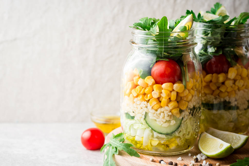 Gezonde zelfgemaakte salades met bulgur, groenten en kalk in mason jars op grijze stenen achtergrond. - Foto, afbeelding