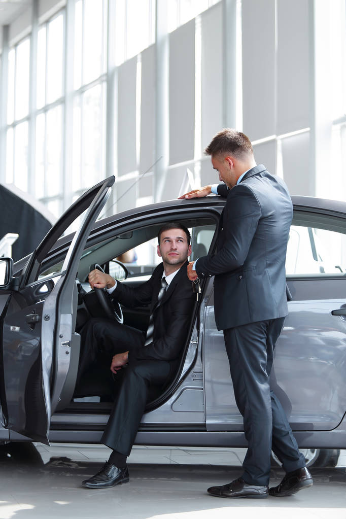 επιχειρηματίας λαμβάνει από τη διαχείριση των κλειδιών, που κάθεται πίσω από το τιμόνι ενός νέου αυτοκινήτου. - Φωτογραφία, εικόνα