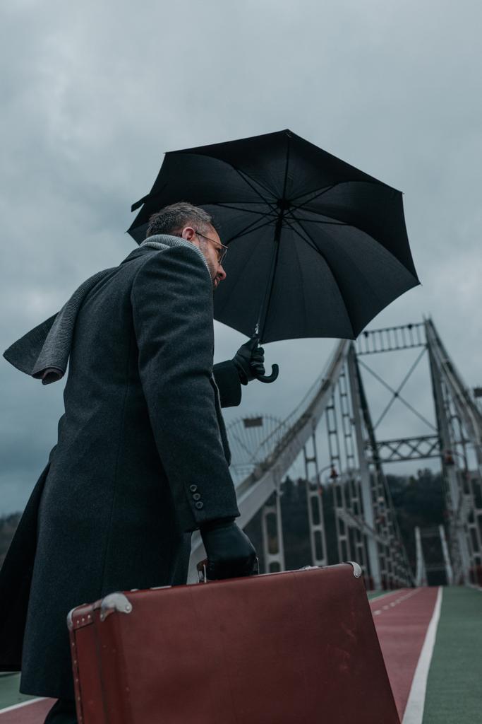vista in basso dell'uomo di mezza età con ombrellone e bagagli passeggiando sul ponte pedonale
 - Foto, immagini