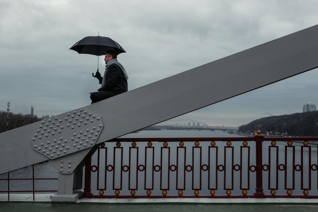 yksinäinen mies sateenvarjo istuu sillan rakentaminen
 - Valokuva, kuva