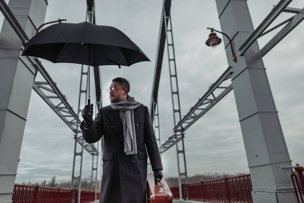 einsamer erwachsener Mann mit Regenschirm und Gepäck läuft über Brücke - Foto, Bild