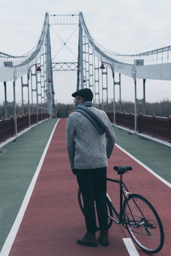 вид сзади стильного человека с велосипедом, стоящим на пешеходном мосту
 - Фото, изображение