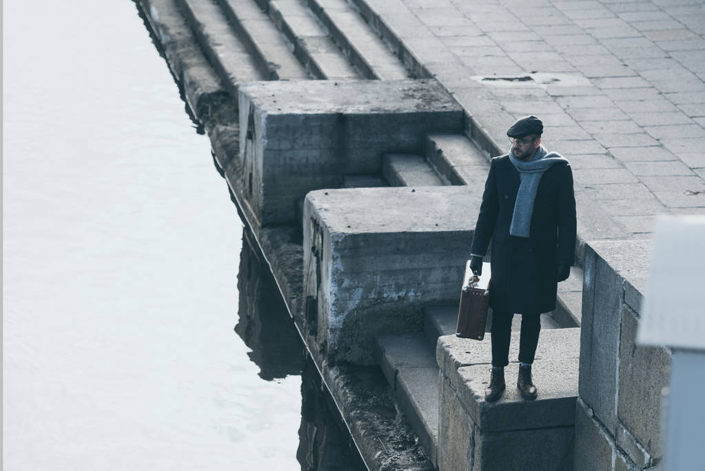 μεγάλη γωνία προβολής του ενήλικα ανθρώπου με βαλίτσα στέκεται στην όχθη του ποταμού - Φωτογραφία, εικόνα