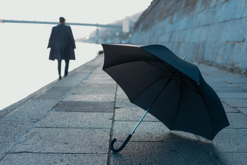 зонтик лежит на берегу реки, в то время как человек идет размытый на заднем плане
 - Фото, изображение