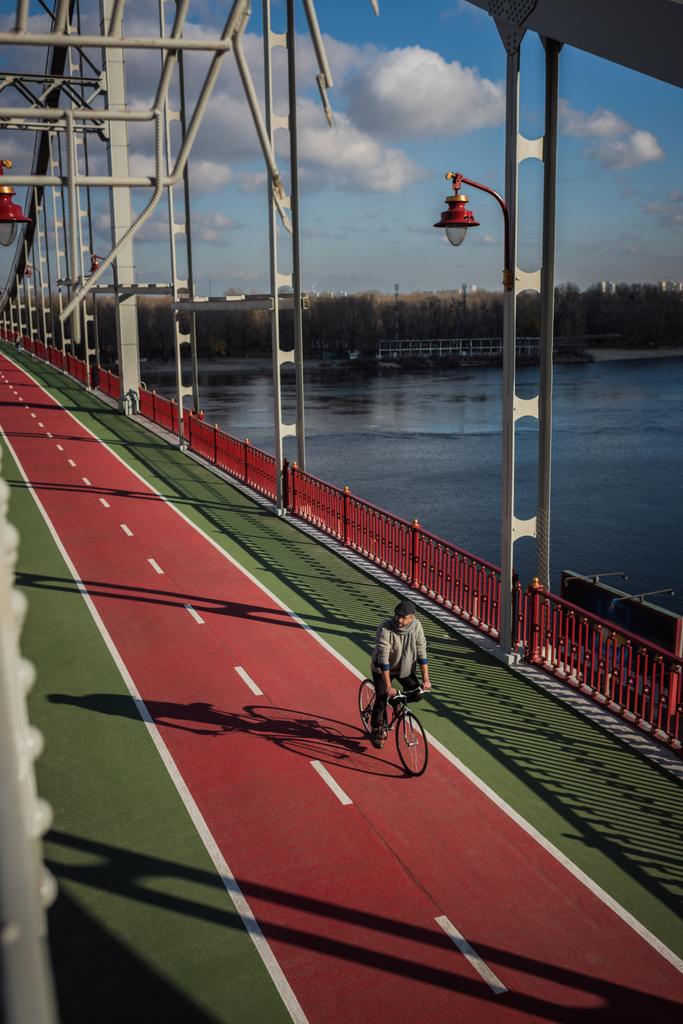 bir yetişkin adam Nehri üzerinde yaya köprüsü üzerinde bisiklet sürme yüksek açılı görünüş - Fotoğraf, Görsel