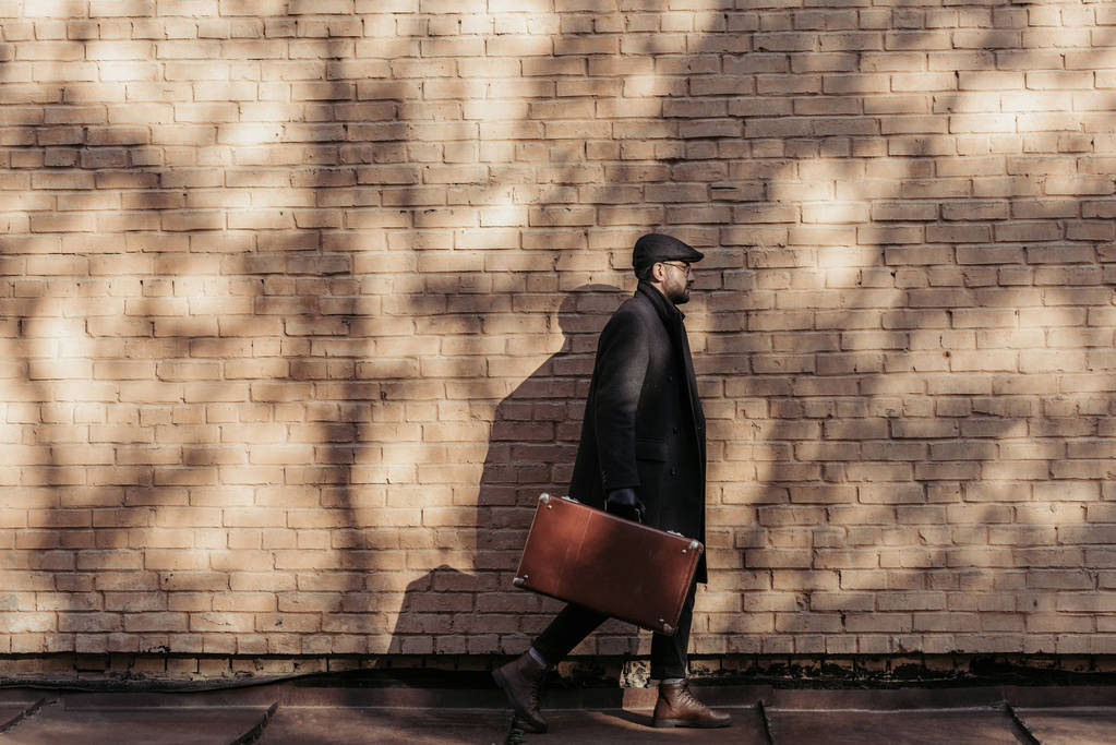 vista lateral del hombre adulto con la maleta caminando delante de la pared de ladrillo
 - Foto, imagen