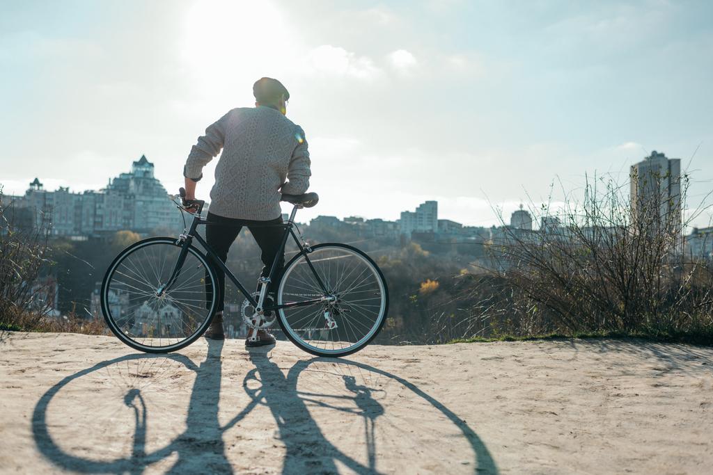πίσω όψη του καλαίσθητο άνθρωπος κάθεται στο ποδήλατο και να βλέπουν την πόλη - Φωτογραφία, εικόνα