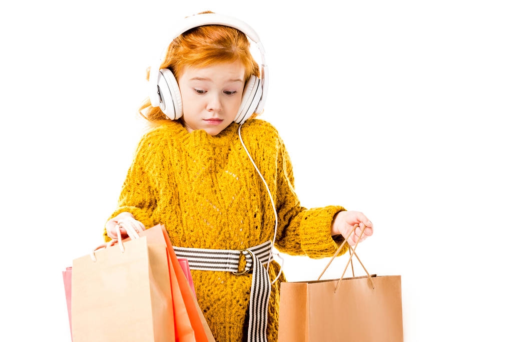 Überraschtes Rothaarkind blickt auf Einkaufstüten in weißen Händen  - Foto, Bild